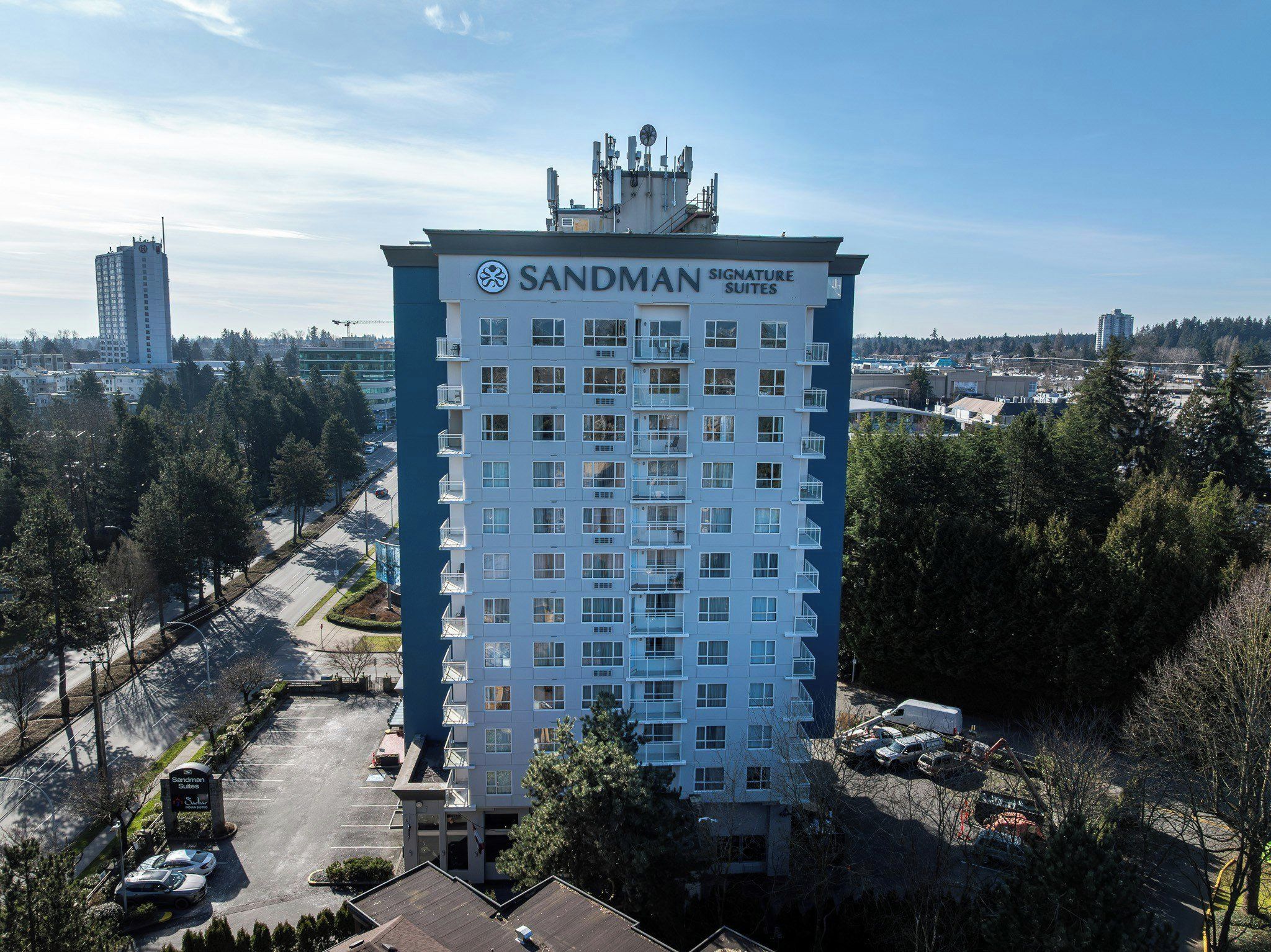 A high-rise hotel with multiple floors, a prominent sign reading 'Sandman Signature Suites,' and a parking area in front.