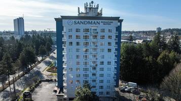 A high-rise hotel with multiple floors, a prominent sign reading 'Sandman Signature Suites,' and a parking area in front.