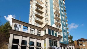A multi-story building with a rooftop patio sign, a ground-level entrance labeled 'SARKAR,' and a parking lot. - Sandman Signature Surrey-Guildford Suites (Surrey)
