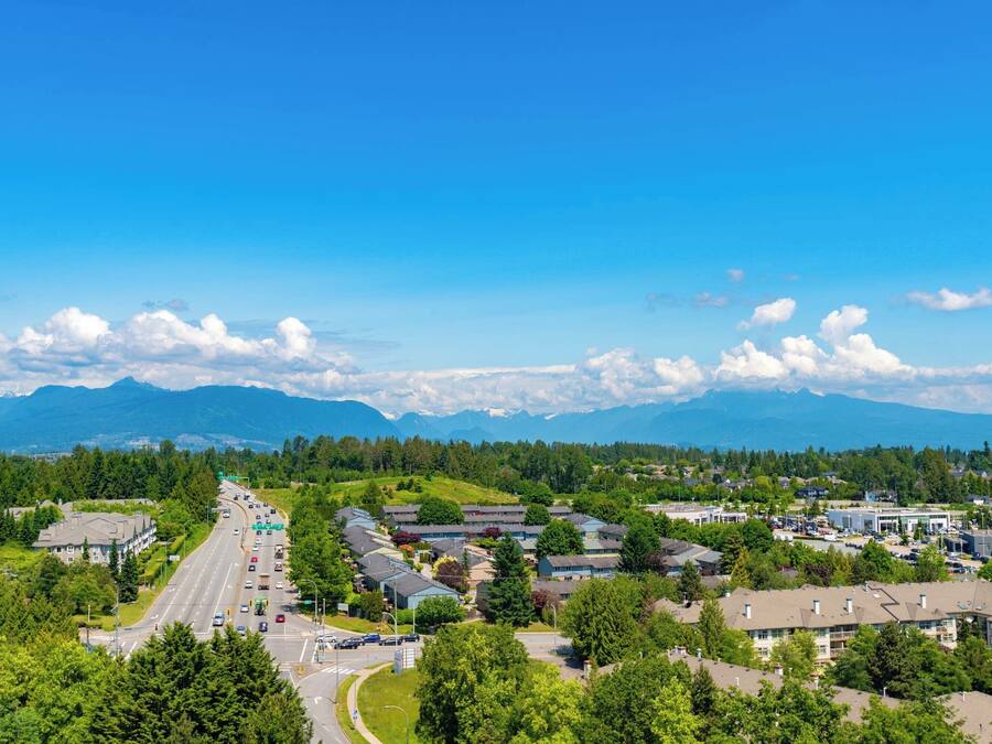 A residential area with a main road, houses, and a mountain range in the background.