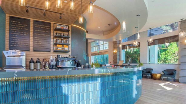 A modern bar area with a menu board, coffee machines, and seating with a view. - Sandman Signature Surrey-Guildford Suites (Surrey)