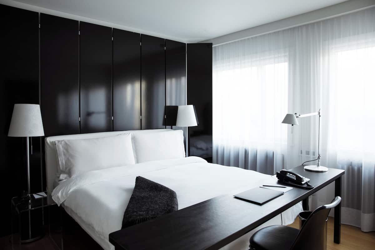 Una habitación de hotel moderna con una cama grande, un escritorio con lámpara y una silla.
