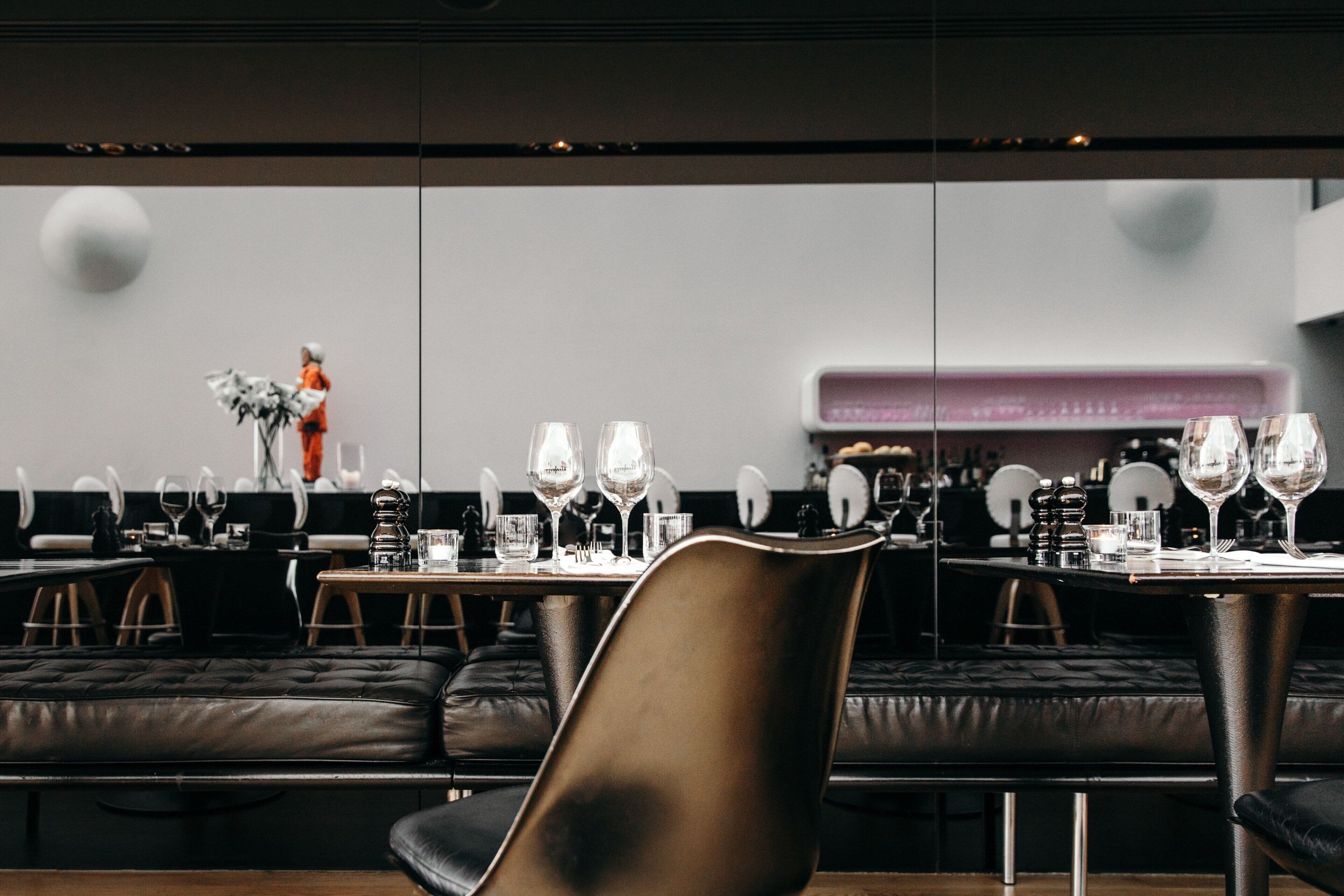 Un comedor moderno con asientos de cuero, mesas dispuestas con copas de vino y cubiertos, y una decoración minimalista.