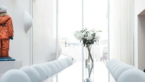 Ein modernes Interieur mit einem weißen Tisch, einer Vase mit weißen Blumen und einer Skulptur links.