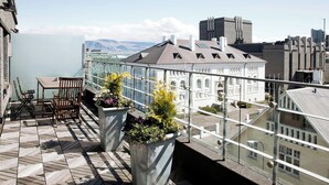 Ein Balkon mit Tisch und Stühlen, Topfpflanzen und Blick auf ein Gebäude mit der Aufschrift 'ARRA'.