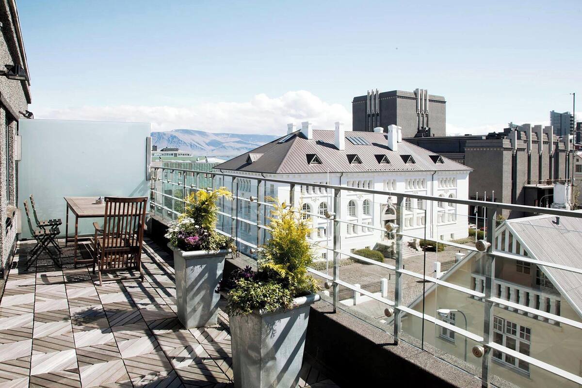 Un balcón con una mesa y sillas, plantas en macetas y vistas de un edificio con un letrero que dice "ARRA".