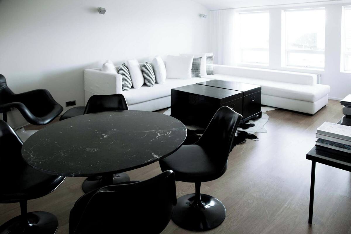 Una sala de estar moderna con un sofá blanco, sillas negras, una mesa redonda negra y una mesa de centro negra.