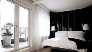 Ein Schlafzimmer mit einer großen Glasschiebetür, die auf einen Balkon führt, einem Bett mit weißer Bettwäsche und zwei Wandleuchten.