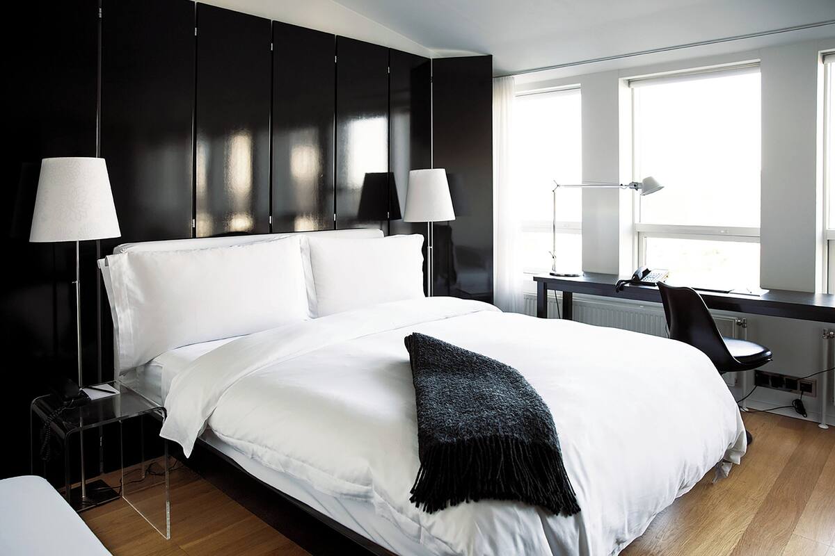Una habitación de hotel moderna con una cama grande, dos lámparas de noche, un escritorio y una silla.