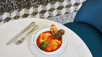 Un tazón de cerámica blanca con salsa roja, adornado con hierbas, sobre una mesa blanca con un cojín azul.