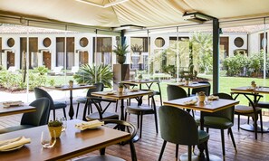 An outdoor dining area with tables and chairs, surrounded by glass walls and a view of a garden.