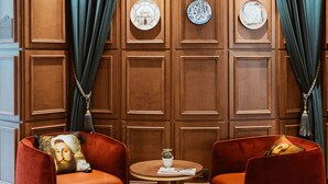 Ein Zimmer mit zwei roten Samt-Sesseln, einem kleinen runden Tisch und einer Holzwand mit dekorativen Tellern und Vorhängen.