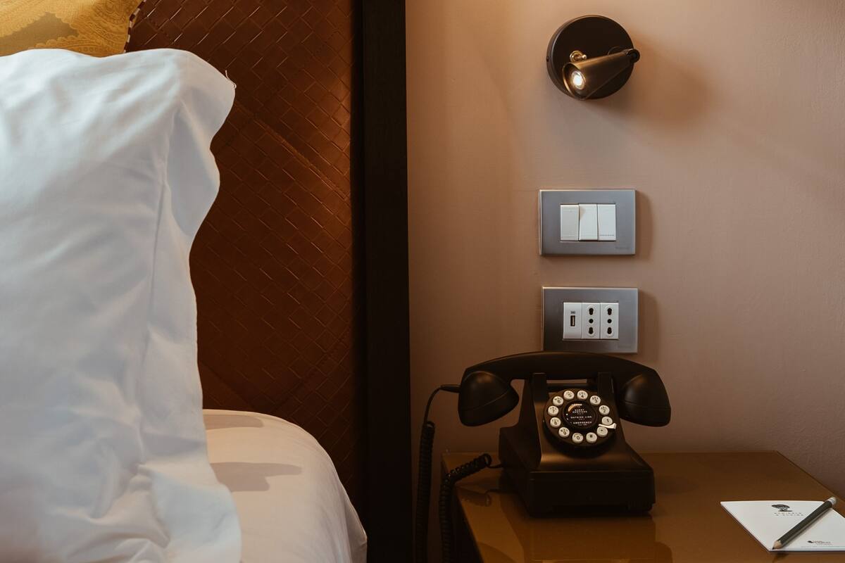 Une chambre d’hôtel avec un lit, une table de chevet dotée d’un téléphone à cadran et deux interrupteurs d’éclairage fixés au mur.