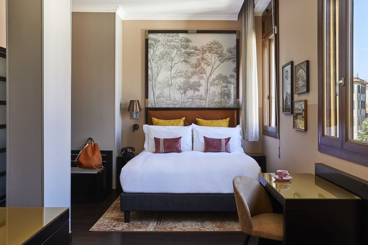 Une chambre d’hôtel avec un lit, un bureau, une chaise, une lampe et un tableau au mur.
