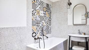 Ein Badezimmer mit freistehender Badewanne, einem wandmontierten Waschbecken und einer dekorativen Fliesenrückwand.