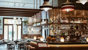 Eine Bar mit einer hohen Theke, mehreren hängenden Pendelleuchten und einer Auswahl an Flaschen und Gläsern in Regalen.
