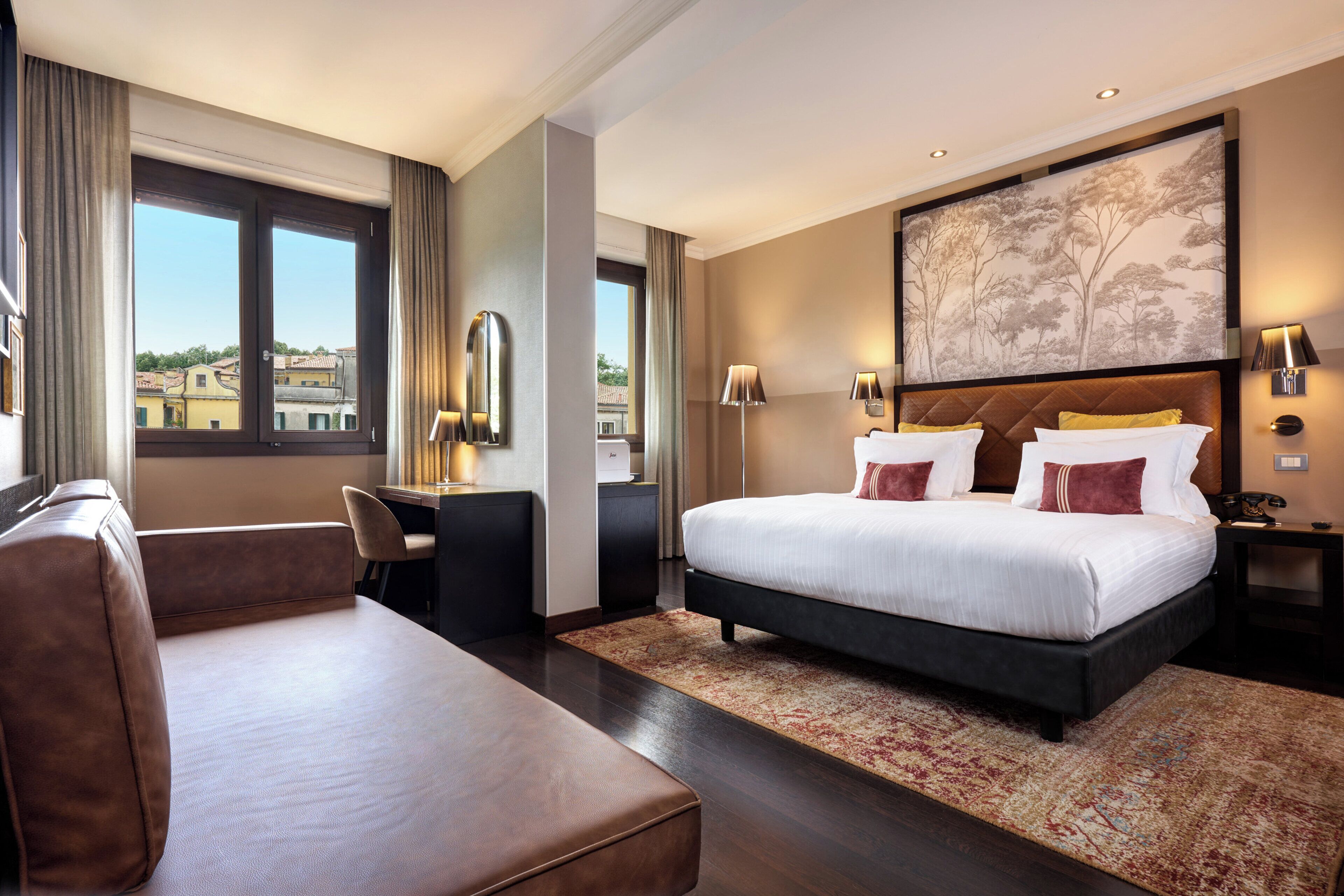 Ett hotellrum med en stor säng, en soffa, ett skrivbord och utsikt över staden.