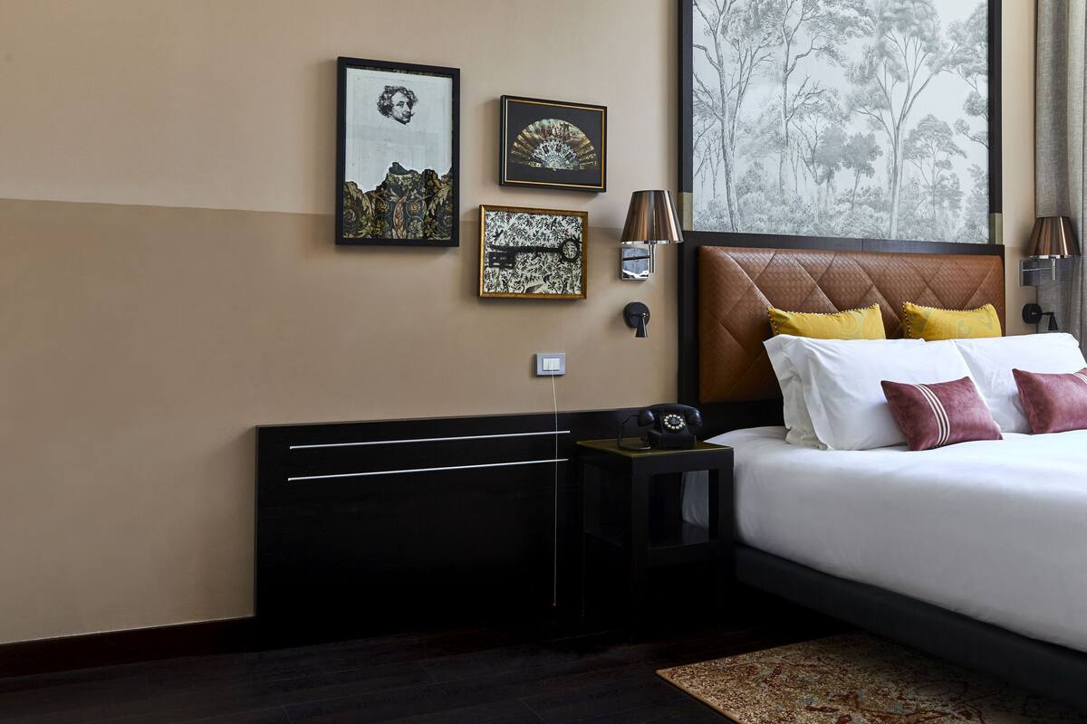 Une chambre d’hôtel avec un lit, des tables de chevet, des œuvres d’art encadrées et une grande fenêtre donnant sur la forêt.