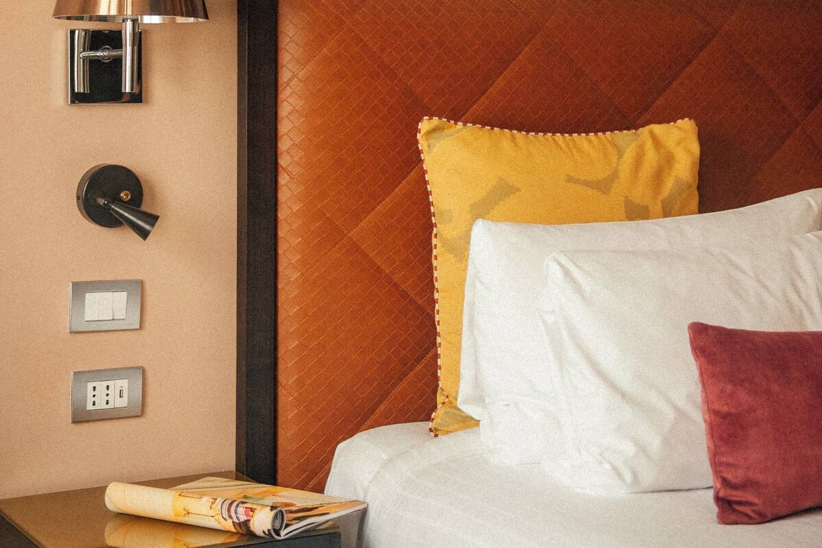 Ein Hotelzimmer mit einem Bett, einem Nachttisch, einer Lampe und einer Wand mit einem Baum-Wandbild.