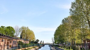 Ein Kanal mit einer Brücke, umgeben von Bäumen und einem Gebäude mit Zäun.
