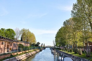 Un canal surmonté d’un pont, bordé d’arbres et adjacent à un bâtiment entouré d’une clôture.