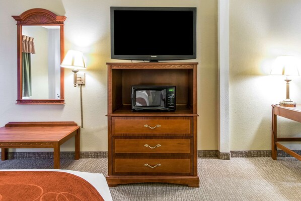Une chambre d’hôtel équipée d’une commode en bois, d’un téléviseur à écran plat, d’un four à micro-ondes, d’un miroir et de deux lampes.