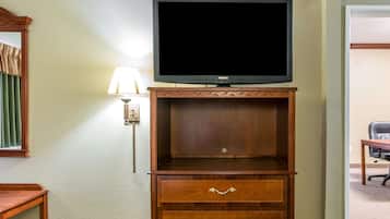 Et hotelværelse med fjernsyn på et træstel, en lampe og et skrivebord med stol.