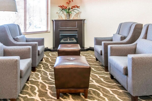 A room with four grey armchairs, a brown leather ottoman, and a fireplace with a vase of flowers.