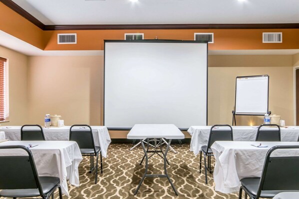 Une salle de conférence équipée de tables, de chaises, d’un tableau blanc et d’un écran de projection.