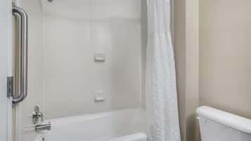 Une salle de bain avec une baignoire blanche, des toilettes, une douche avec un rideau blanc et une barre d’appui.