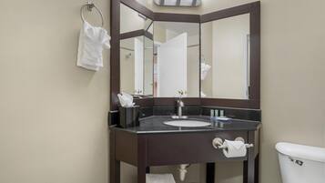 Un baño con tocador de madera oscura, un lavamanos blanco, un espejo y un inodoro.