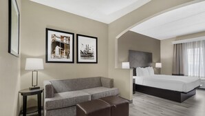 A hotel room with a bed, a sofa, an ottoman, a side table, and two framed pictures on the wall.