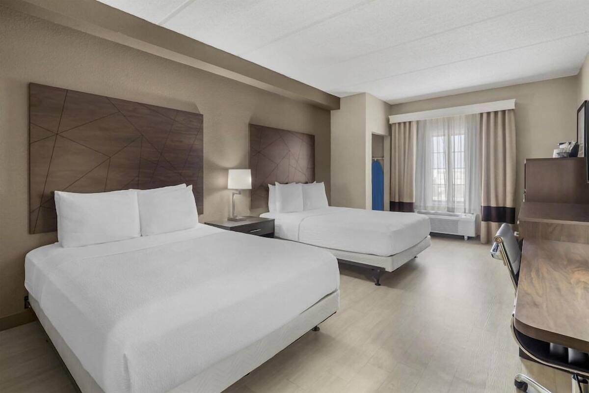 Une chambre d’hôtel avec deux lits, un bureau, une chaise, une télévision et une fenêtre avec des rideaux.