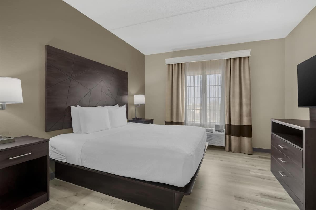Une chambre d’hôtel avec un grand lit, des tables de chevet, une télévision et une fenêtre avec des rideaux.
