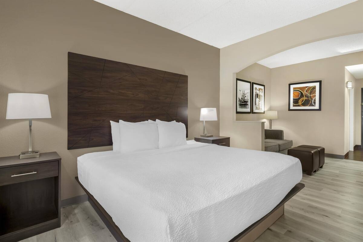 Une chambre d’hôtel avec un grand lit, deux tables de chevet avec des lampes, une tête de lit, un canapé et des œuvres d’art accrochées aux murs.
