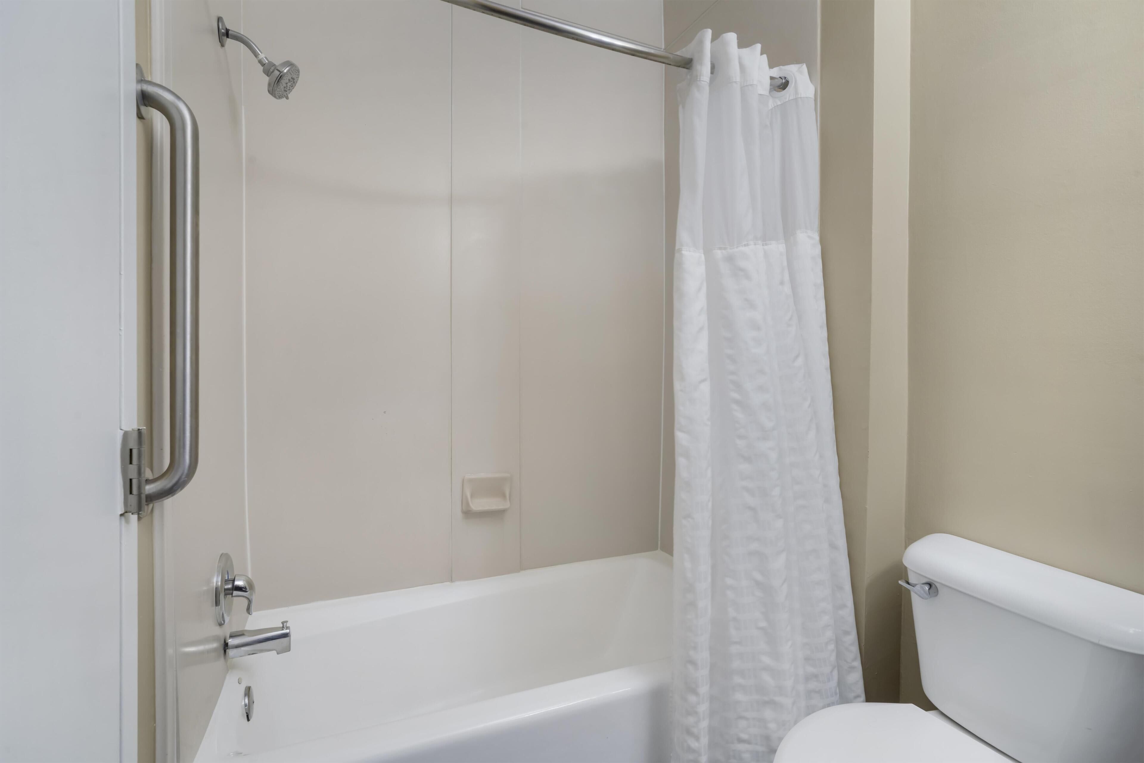 Une salle de bain équipée d’une baignoire, de toilettes, d’un rideau de douche et de barres d’appui.