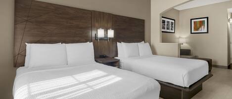 A hotel room with two beds, a wooden headboard, bedside lamps, a nightstand, and framed pictures on the wall.