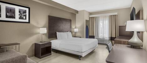 Habitación de hotel con cama, mesitas de noche, escritorio, silla, televisor y cuadros en la pared.