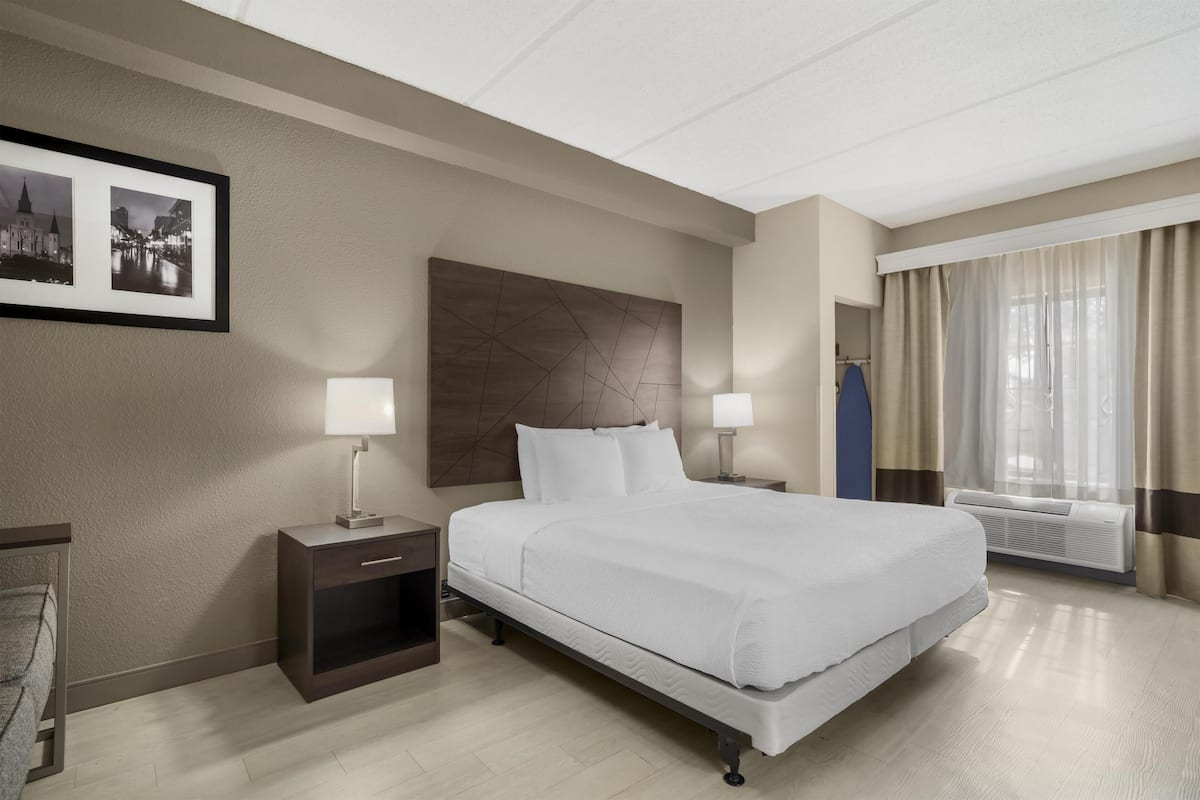 Une chambre d’hôtel avec un lit, des tables de chevet avec des lampes, un tableau encadré au mur et une fenêtre avec des rideaux.