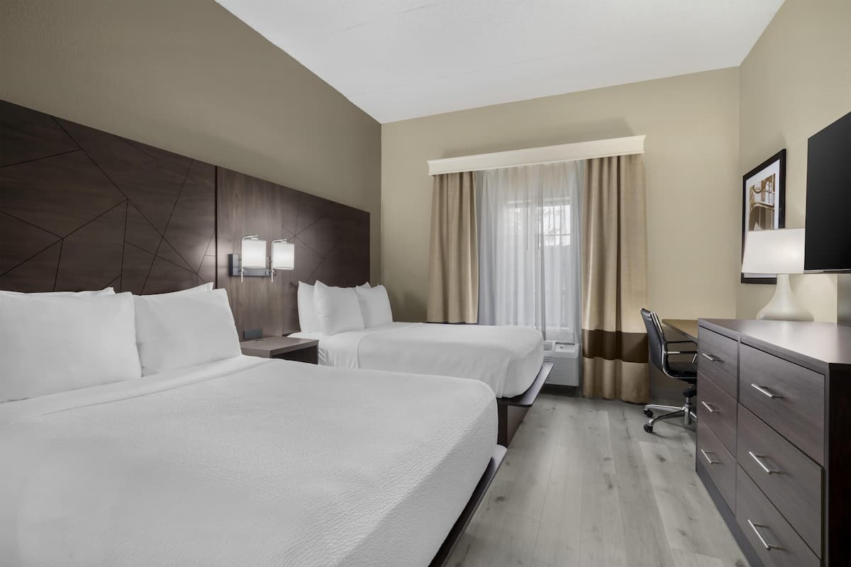 Une chambre d’hôtel avec deux lits, un bureau, une chaise, une commode et un téléviseur.