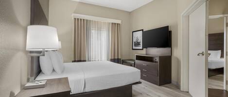 Habitación de hotel con cama, mesita de noche, lámpara, televisión y puerta que da a otra estancia.