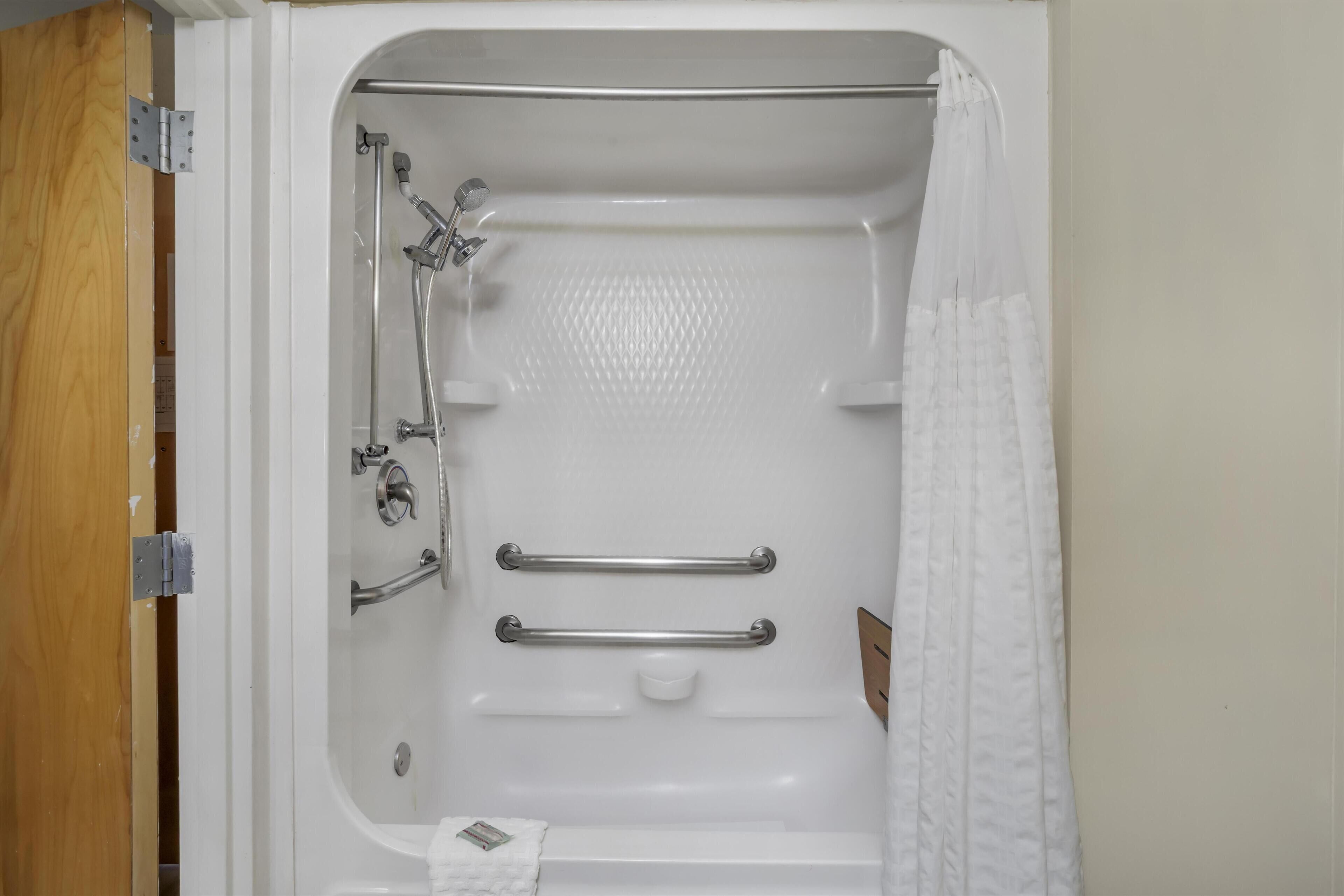 Une baignoire blanche équipée d’une pomme de douche, de barres d’appui et d’une serviette.