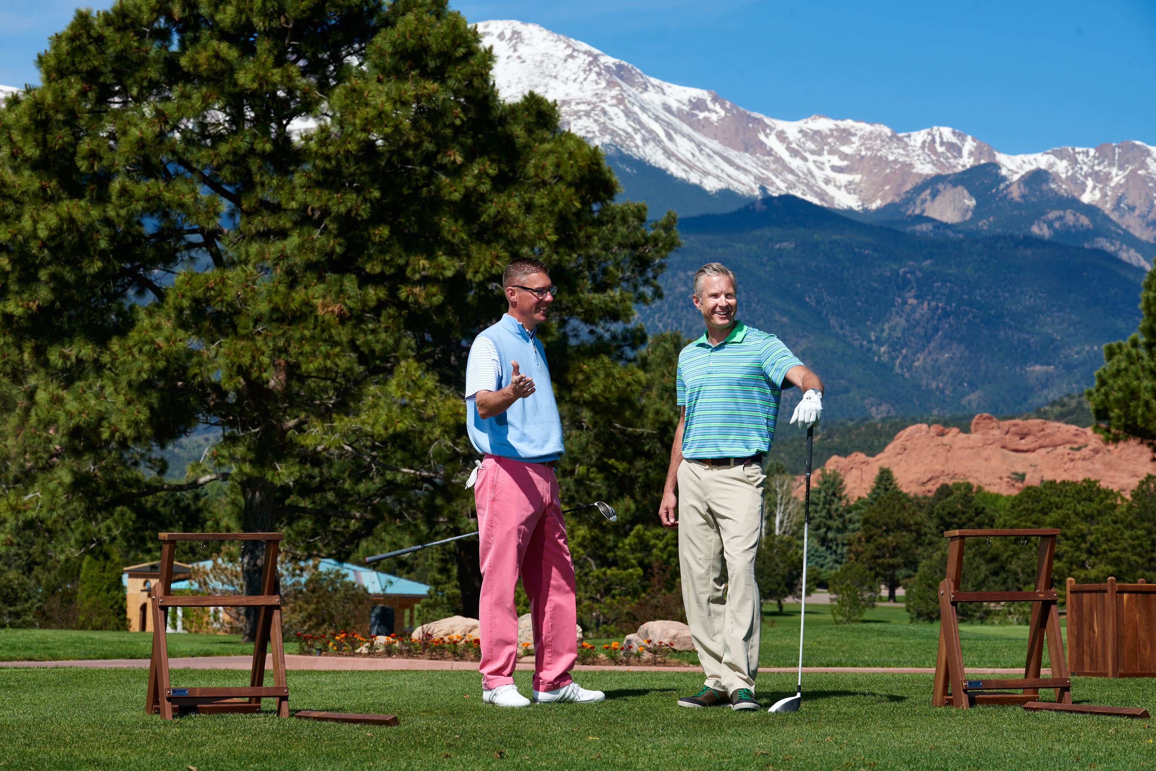 Two people standing on a golf course with a mountainous backdrop.