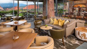 A spacious indoor area with multiple seating arrangements, a bar, and large windows offering a view of red rock formations. - Garden of the Gods Resort and Club (Colorado Springs)