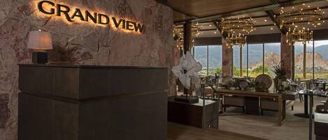 A reception area with a stone wall, a 'GRAND VIEW' sign, a reception desk, and a seating area with a view of the mountains.