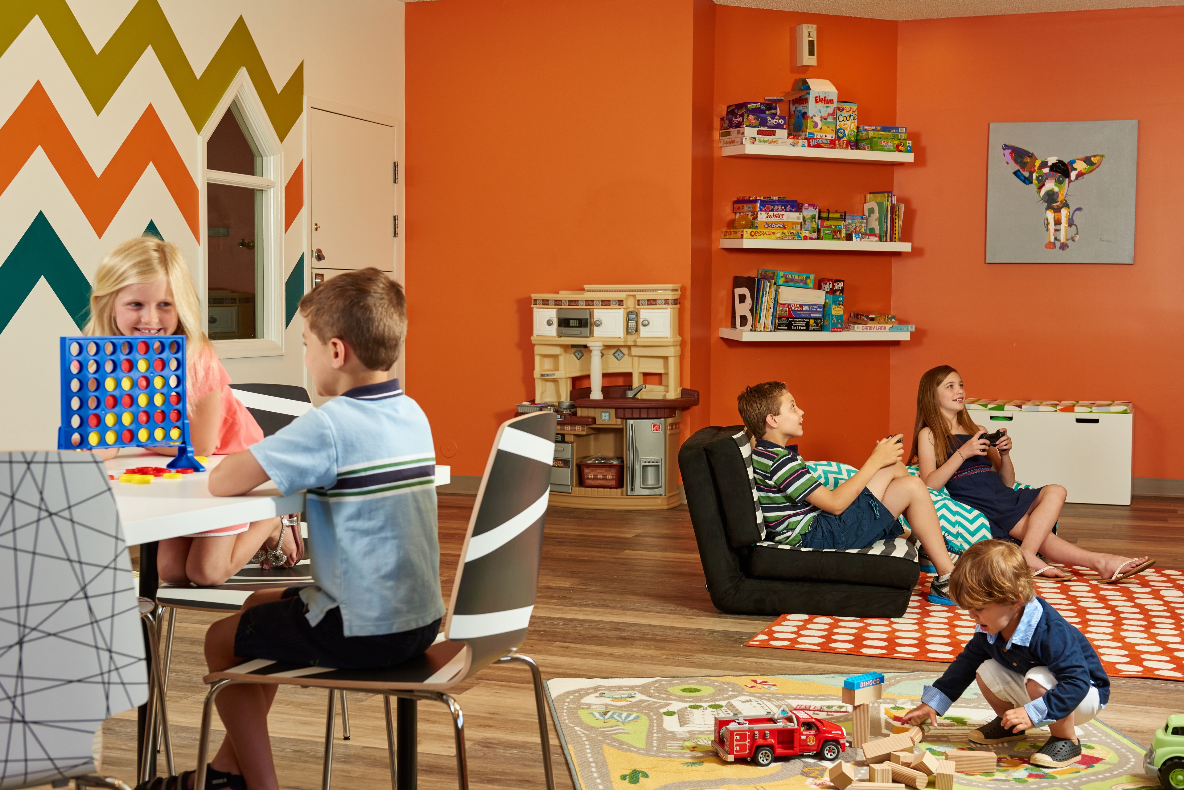 Une pièce avec un mur orné d’un motif en chevrons, un espace de jeux avec des jouets, et des étagères remplies de livres et de jeux.