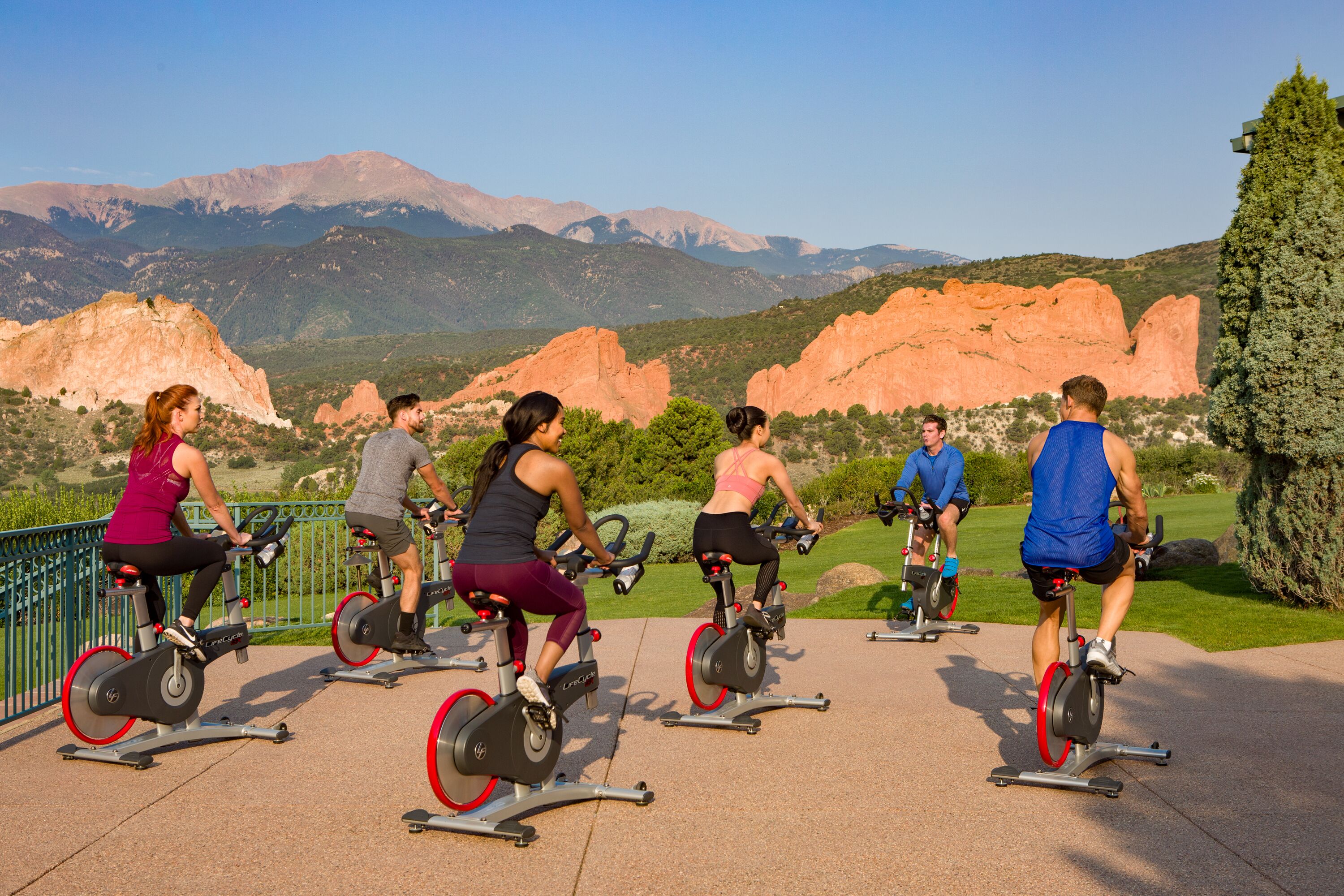 A group of people on stationary bikes in an outdoor setting with a mountainous backdrop.
