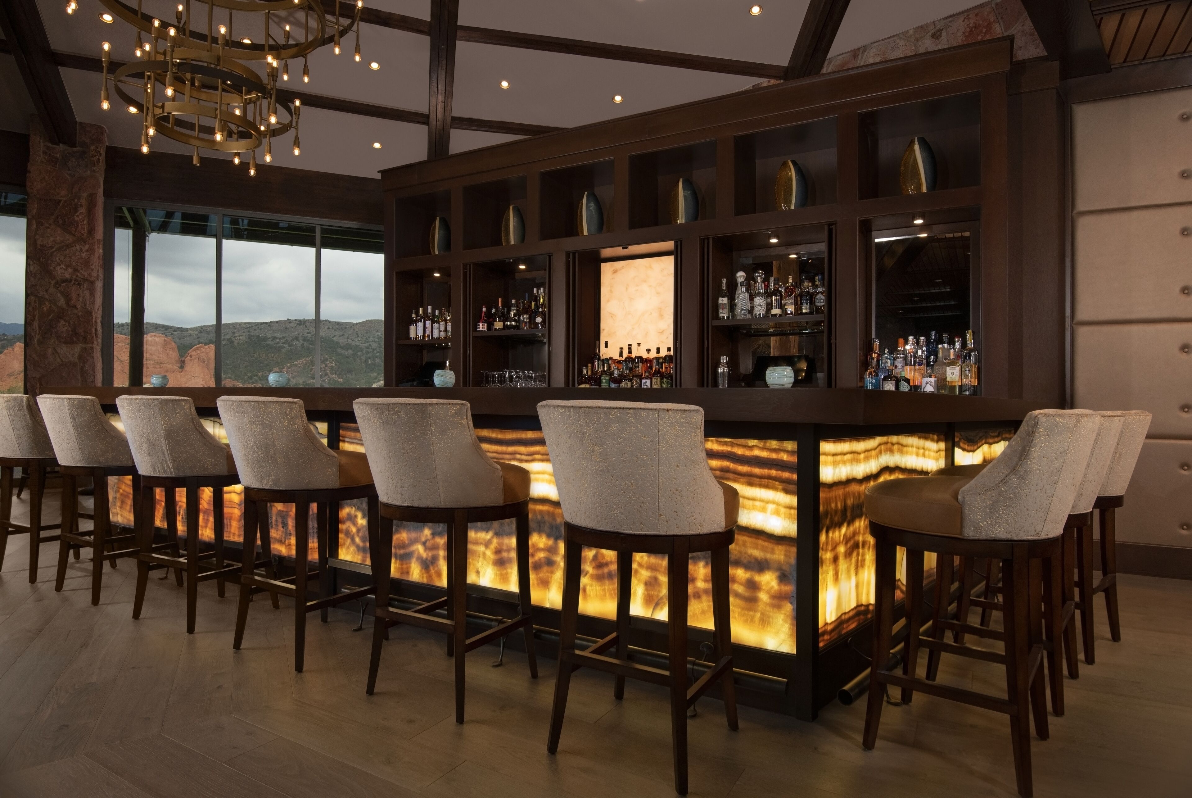 A bar area with a long counter, multiple stools, and shelves with bottles.