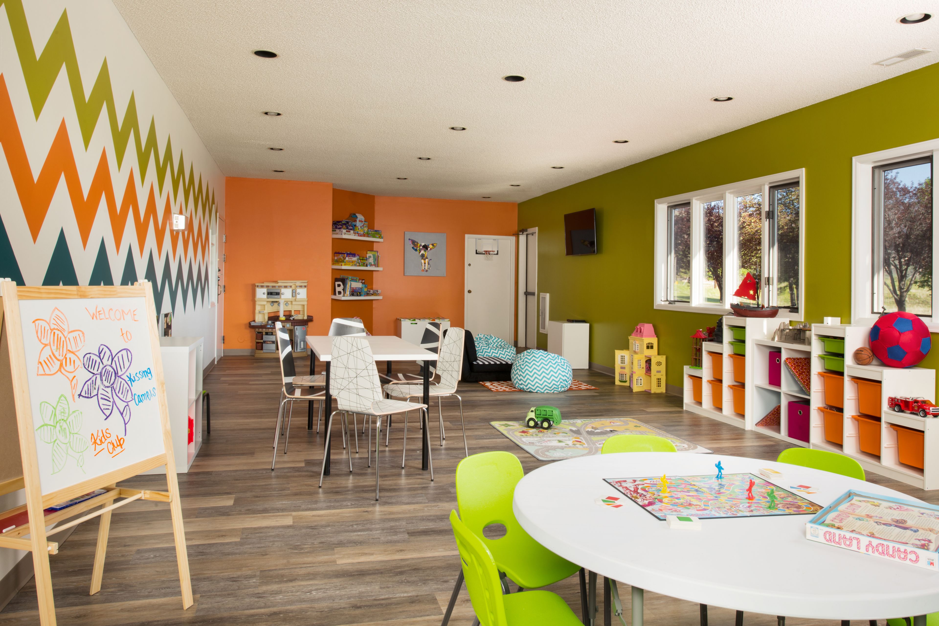 Una vivace sala giochi per bambini con lavagna, tavoli, sedie e contenitori portaoggetti.