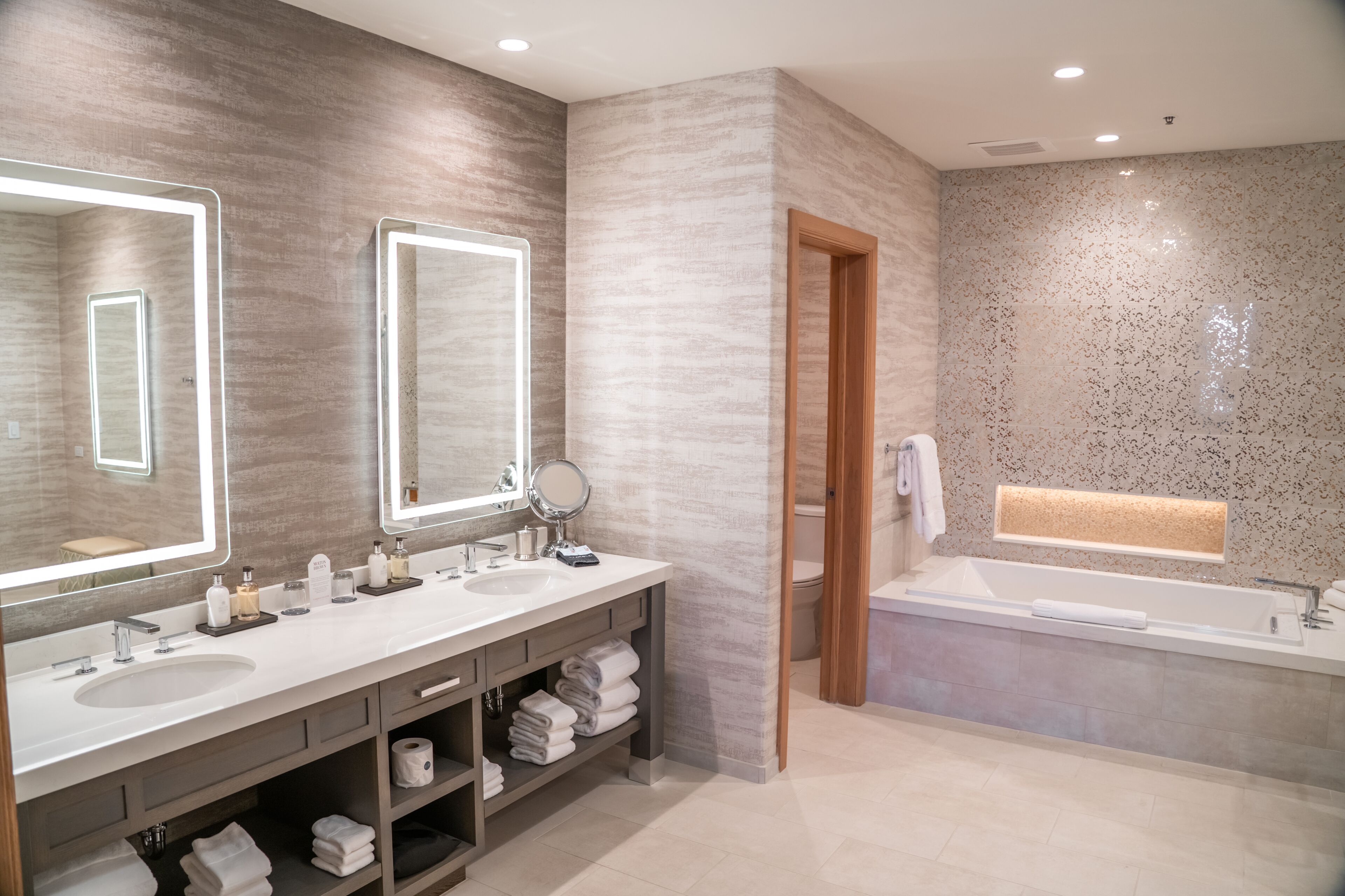 A modern bathroom with two sinks, a large mirror, a bathtub, and a towel rack.